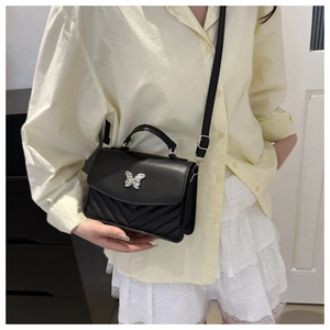 Detail of black quilted mini square bag featuring a silver butterfly buckle and top handle