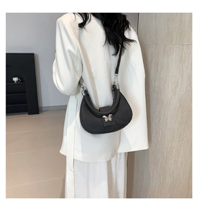 Détail d'un sac demi-lune noir avec boucle papillon argentée sur blazer blanc