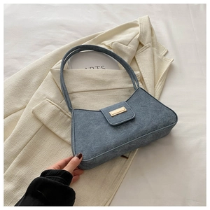 Blue denim shoulder bag with a gold rectangular buckle on a beige blazer setting
