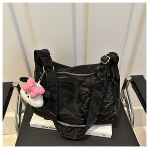 Détail du sac cabas plissé noir avec breloque en peluche posé sur un livre blanc