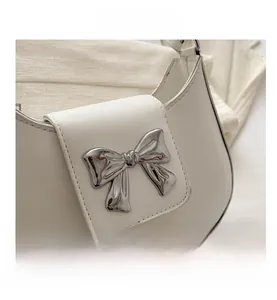 Detailed close-up of white leather shoulder bag with a silver bow metal accessory