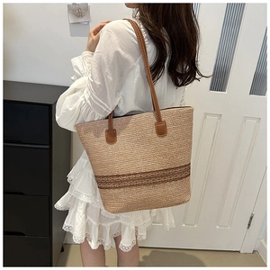 Side view of a woven straw tote bag with brown leather straps and decorative stripes