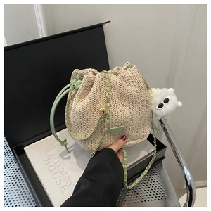 Detail of straw bucket bag with green leather trim, chain strap and plush monster charm