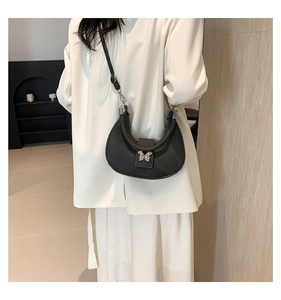 Détail du sac hobo croissant noir avec boucle papillon argentée sur un blazer blanc