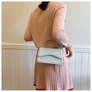 Silver sequin handbag shown on model side-view with detachable strap and metallic finish
