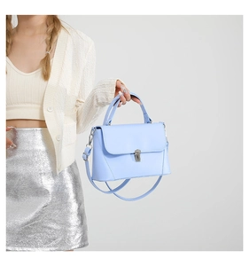 Detail of light blue trapezoid handbag with silver hardware on model in white cardigan