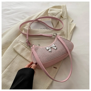Detailed view of pink rhinestone crescent bag with metallic bow buckle on a beige blazer