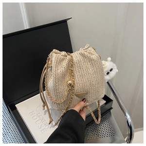Detail of beige straw bucket bag with gold chain strap and cute monster charm