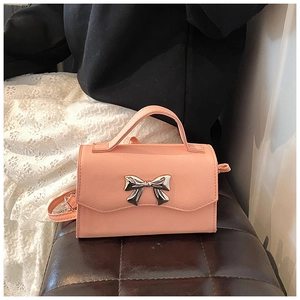 Detailed shot of a pink mini crossbody bag with a silver metal bow on a leather seat