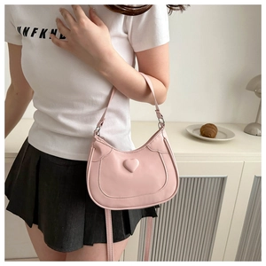 Pink heart saddle bag detail shown as an underarm shoulder bag on a model