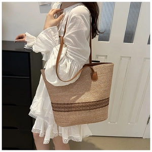 Detail of large woven straw tote bag with brown leather straps for summer beach travel