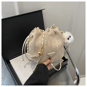 Close-up of beige straw bucket bag with gold chain strap and plush pendant detail