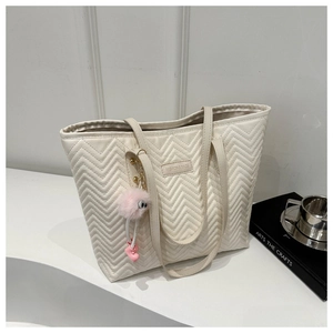 Detail of cream tote bag featuring herringbone quilting and pink plush ball charm