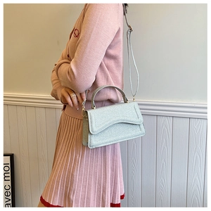 Detail of silver sequined handbag featuring a metallic flap and curved top handle