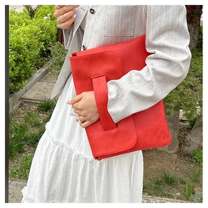 Detail of red PU leather envelope clutch with textured finish and wide handle strap