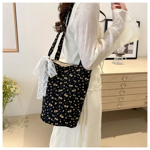 Detail shot of a black floral tote bag with a white lace bow on the shoulder strap