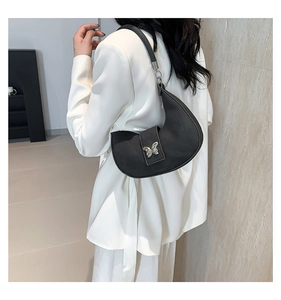 Dettaglio borsa hobo nera con fibbia a farfalla argentata indossata su blazer bianco