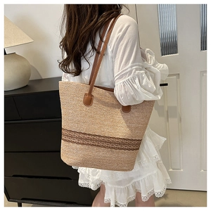Detail of straw woven tote bag featuring brown leather handles and a two-tone texture