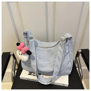Détail d'un sac cabas plissé bleu clair avec un charm en peluche rose sur une chaise