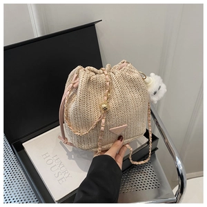 Close-up of beige straw bucket bag with pink leather trim and chain shoulder strap
