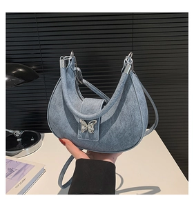 Détail du sac croissant bleu denim avec boucle papillon argentée et texture de tissu fine