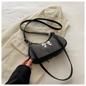 Close-up of black crescent shoulder bag featuring silver rivets and metal bow detail