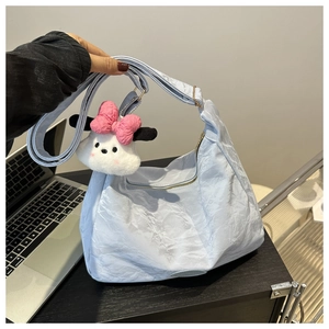 Détail du cabas plissé bleu ciel avec un charm chiot en peluche blanc et bandoulière large