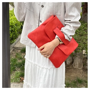 Détail d'un sac à main rouge en cuir texturé avec large poignée intégrée et rabat