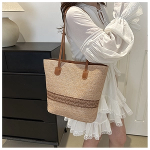 Detail of hand-woven straw tote bag with brown leather straps and striped accents