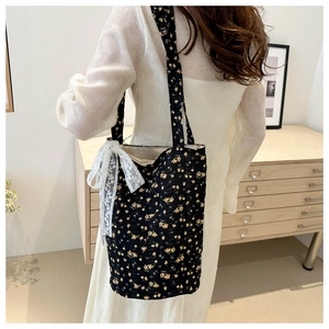 Floral print black tote bag with white lace bow detail shown on model in home setting