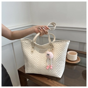 Close-up of white quilted tote bag with fashion label and pink plush monster charm