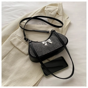 Detail of a black rhinestone hobo bag with silver bow accent on beige blazer
