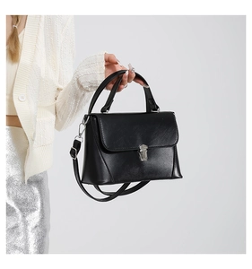 Detail view of black glossy leather bag with silver twist lock and detachable shoulder strap