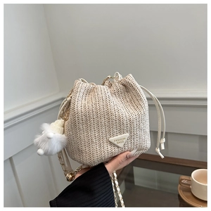 Detail of woven straw bucket bag with drawstring closure and plush ball charm