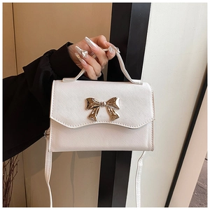 Detail showing cream-colored textured leather square bag with golden bow and top handle