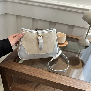 Chic beige canvas crossbody bag with silver metallic accents and gold buckle on a table