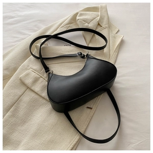 Minimalist black half-moon shoulder bag with adjustable strap on a textured background