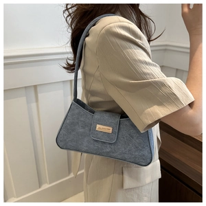 Blue denim baguette shoulder bag with gold buckle shown on model in a modern room