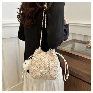 Detail of beige woven bucket bag with V-shaped texture, chain strap, and pompom charm