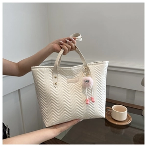 Detail of off-white quilted tote bag with V-shaped stitching and plush charm accessory