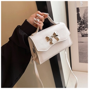 Close-up of white crossbody bag with cross-grain leather and gold bow buckle detail