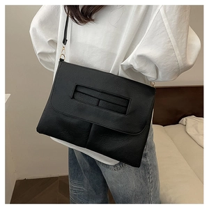 Detail of black textured leather crossbody bag with chain strap and modern rectangle flap