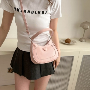 Pink heart-shaped embossed shoulder bag with adjustable straps in a minimalist indoor setting