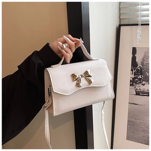 Detail of white crossbody bag with cross-grain texture and gold bow metal clasp