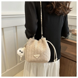 Detail of beige straw bucket bag featuring drawstring closure and white plush charm
