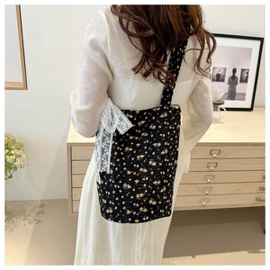 Detail of floral canvas crossbody bag featuring delicate white lace bow decoration