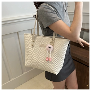 Detailed view of white quilted tote bag with V-pattern stitching and pink plush charm