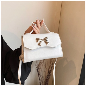 Close-up of white cross-grain leather bag with a decorative golden metal bow detail