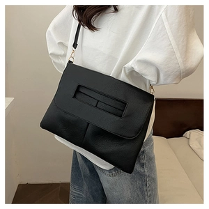 Détail d'un sac bandoulière en cuir noir avec poignée découpée rectangulaire et boucles dorées
