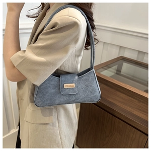 Detail of denim blue baguette shoulder bag with gold clasp shown on model